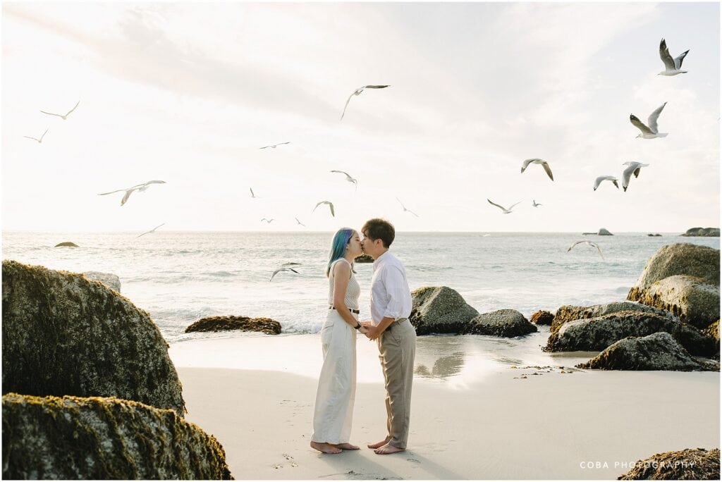 Engagement beach photo of Yutaro and Rei walking along Camps Bay shoreline at sunset